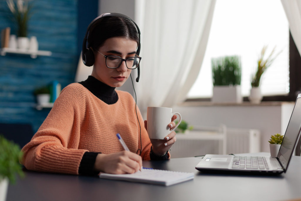 Student with headphones listening to online course and taking notes